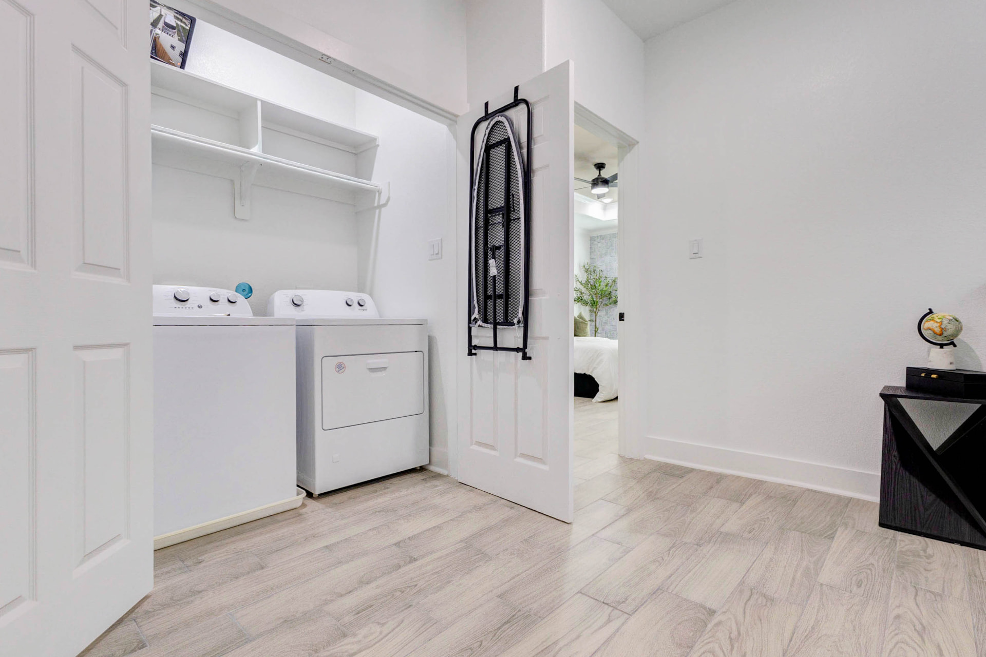 Laundry closet with washer, dryer, shelving and ironing board beside a guest bedroom